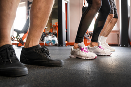 Trois personnes en tenue de sport effectuent des exercices au sol dans une salle de fitness, leurs pieds en mouvement suggérant un entraînement dynamique ou une séance de groupe.