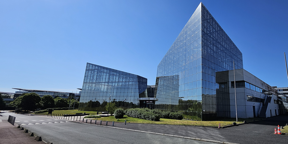 Un bâtiment emblématique du Futuroscope aux formes géométriques audacieuses, entièrement recouvert de façades vitrées réfléchissantes qui jouent avec la lumière et le ciel bleu, dans un cadre paysager soigné.