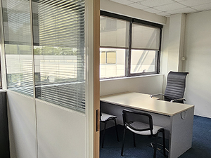 Un bureau lumineux et fonctionnel, équipé d’un grand bureau clair, de trois chaises dont une de direction, avec de larges fenêtres et des cloisons vitrées donnant sur le couloir.