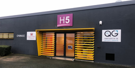 Entrée d’un bâtiment moderne et sobre identifié par le panneau “H5”, avec une porte encadrée de lames jaunes et des enseignes signalant un espace dédié au sport, à la santé et à la qualité de vie.